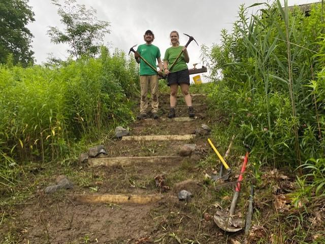 斯特拉和雅各布站在他们刚建好的楼梯间里，手里拿着工具.